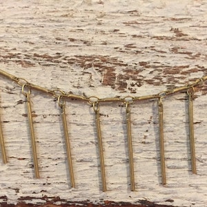 May include: A gold chain necklace with multiple dangling gold bars. The necklace is on a white wooden background.