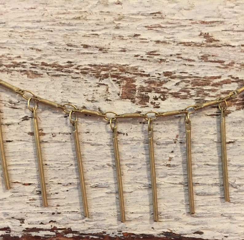 May include: A gold chain necklace with multiple dangling gold bars. The necklace is on a white wooden background.