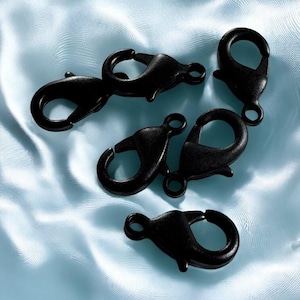 May include: A collection of black lobster claw clasps, arranged on a light blue satin fabric. The clasps are made of metal and have a matte finish. They are designed for jewelry making or crafting projects.