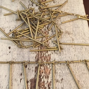 May include: A gold chain with multiple gold metal rods hanging from it. The chain and rods are on a white wooden surface.