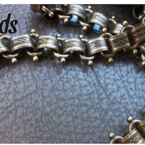 May include: Gold chain with intricate details and small round accents. The chain is made of metal and has a textured finish.