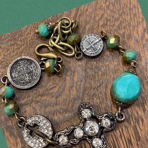 Puede incluir: Un brazalete turquesa y plateado con un dije de cruz, cuentas turquesas y una medalla de San Cristóbal.