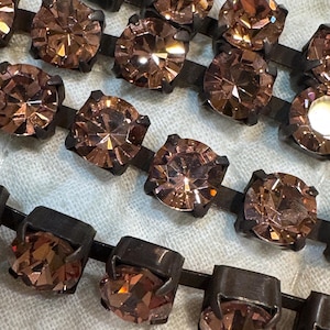 Puede incluir: Primer plano de una cadena de diamantes de imitación marrones engastados en engastes de metal negro. Los diamantes de imitación son facetados y tienen un acabado brillante.