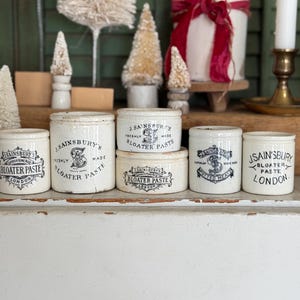 May include: A collection of vintage J. Sainsbury's Bloater Paste jars. The jars are white with black text and illustrations. The jars vary in size and shape, with some having lids. The text on the jars includes "J. Sainsbury's", "Bloater Paste", and "London".