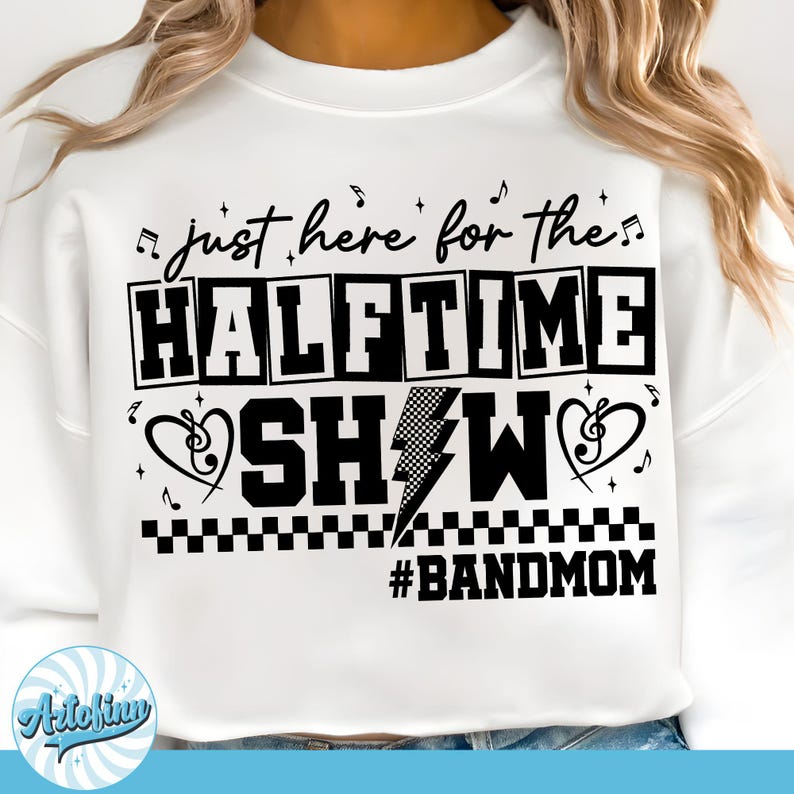May include: White sweatshirt with the text "just here for the HALFTIME SHOW #BANDMOM" in black. The design includes musical notes, a lightning bolt, and a heart-shaped treble clef. The sweatshirt is a casual, comfortable style.