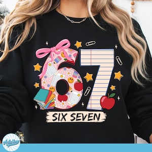 May include: Black sweatshirt with a colorful graphic design featuring the numbers "67" with school-themed illustrations, including books, apples, stars, and the words "SIX SEVEN". A pink bow accents the design.