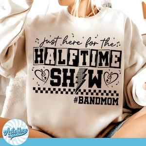 May include: Cream-colored sweatshirt with the text "just here for the HALFTIME SHOW" in black, along with musical notes, hearts, and a lightning bolt graphic. The hashtag #BANDMOM is below the text.