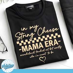May include: Black crew neck t-shirt with the text "in my String Cheese MAMA ERA" in a cursive font. The text includes a checkerboard pattern and the phrase "overwhelmed, touched out but exactly who I'm meant to be".