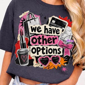 Könnte beinhalten: Ein anthrazitfarbenes T-Shirt mit einer Collage-Grafik und dem Text "we have other options". Das Design zeigt eine Einkaufstasche, eine Kreditkarte, einen Lippenstift, einen Kaffeebecher mit Herz, eine rosa Schleife und herzförmige Sonnenbrillen.