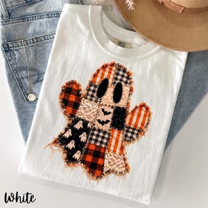 Könnte beinhalten: Ein weißes T-Shirt mit einer großen, zentralen Applikation in Geisterform, die aus verschiedenen Stoffstücken besteht. Die Stoffe zeigen orange-schwarze Karos, schwarz-weiße Vichy-Karos, orange Streifen, Spitze und schwarzen Stoff mit kleinen Geistermotiven.