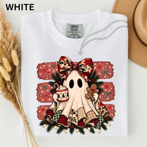 Könnte beinhalten: Ein weißes Kurzarm-T-Shirt mit einer Grafik eines Geistes, der eine große Weihnachtsschleife trägt und eine Tasse mit Zuckerstange und Lebkuchenmann hält, umgeben von Tannenzweigen, roten Schleifen und Sternen auf rotem Hintergrund.