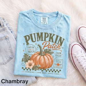 Könnte beinhalten: Ein hellblaues T-Shirt mit einer Grafik eines großen orangefarbenen Kürbisses mit grünen Blättern und dem Text Pumpkin Patch, Fresh From The Patch, Farm Fresh, Locally Grown, Pumpkins, Corn Maze und Apple Cider in Vintage-Schrift.