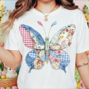 Könnte beinhalten: Ein weißes Kurzarm-T-Shirt mit einer großen Schmetterlingsgrafik, die aus verschiedenen Stoffflicken zusammengesetzt ist. Die Schmetterlingsflügel zeigen eine Mischung aus blauem Denim, rot-weißem Vichy-Karo, hellblauem Karo und Blumenmustern mit ausgefransten Kanten.