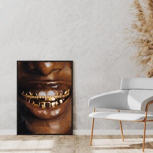 Puede incluir: Una impresi&oacute;n art&iacute;stica enmarcada que presenta un primer plano de una boca sonriente con dientes de oro. Los labios son brillantes y marrones, con un fondo oscuro. La obra de arte se exhibe en una pared junto a una silla blanca.