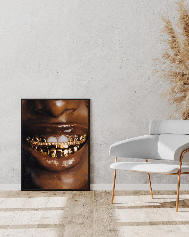 Puede incluir: Una impresi&oacute;n art&iacute;stica enmarcada que presenta un primer plano de una boca sonriente con dientes de oro. Los labios son brillantes y marrones, con un fondo oscuro. La obra de arte se exhibe en una pared junto a una silla blanca.