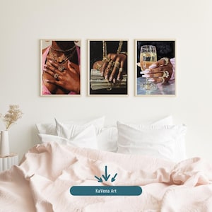 Puede incluir: Tres impresiones artísticas enmarcadas. Una muestra a una persona con joyas de oro y una blusa rosa. Otra muestra manos sosteniendo dinero. La tercera muestra una copa de champán. Las impresiones se muestran sobre una cama.