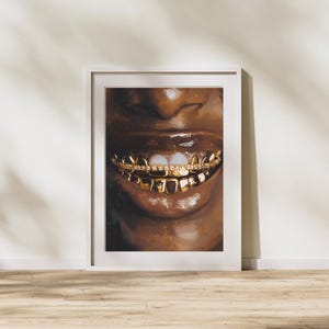 Puede incluir: Una impresi&oacute;n art&iacute;stica enmarcada que presenta un primer plano de una boca sonriente con dientes de oro. La obra de arte muestra los labios y los dientes de una persona, con los dientes de oro brillando contra el tono de piel oscuro. La impresi&oacute;n est&aacute; en un marco blanco.