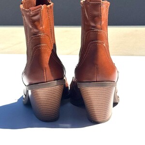 May include: A pair of brown leather ankle boots with stacked heels. The boots have a classic design with a rounded toe and elastic side panels. The heels are approximately 3 inches high, providing a stylish lift.