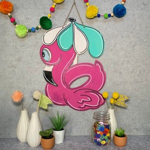 May include: Pink flamingo pool float with a blue and white umbrella, surrounded by colorful buttons and flowers in white vases.