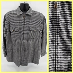 May include: A black and white houndstooth patterned jacket with a full-length zipper and two chest pockets. The jacket has a collared neckline and long sleeves. The zipper pull has a decorative design. The jacket is displayed on a black mannequin.