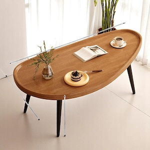 Mesa de centro ovalada moderna de mediados de siglo: madera maciza con patas cónicas, mueble minimalista para sala de estar.