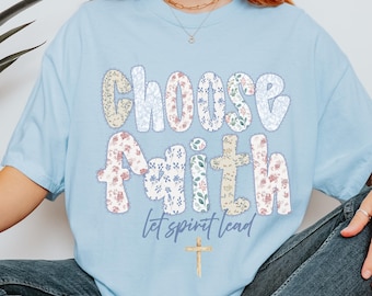 Puede incluir: Camiseta azul claro con las palabras "Choose Faith" en un diseño de patchwork floral. La frase "let spirit lead" y una pequeña cruz están debajo. La camiseta es de estilo casual.