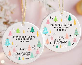 May include: Two white ceramic Christmas ornaments with gold string. Each ornament has a colorful Christmas tree design and the text "TEACHERS LIKE YOU ARE PRECIOUS AND FEW". One says "Love, Ava Smith 2025" and the other says "Love, Oliver 2025".