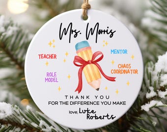 May include: A white round ornament with a pencil design and the text "Mrs. Moris". The ornament includes the words "Teacher", "Mentor", "Role Model", and "Chaos Coordinator". It also says "Thank you for the difference you make, love, Luke Roberts".