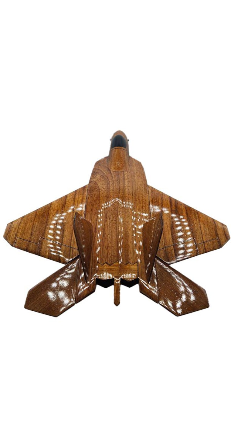 May include: A wooden model of a fighter jet, featuring a detailed design with a brown finish. The wings and body are intricately carved, showcasing the craftsmanship. The jet has a sleek, modern appearance.