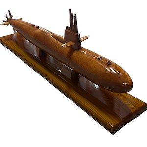 May include: A wooden model of a submarine, featuring a polished, glossy finish. The submarine is brown and rests on a rectangular wooden base. The model includes detailed features like a conning tower and propellers.