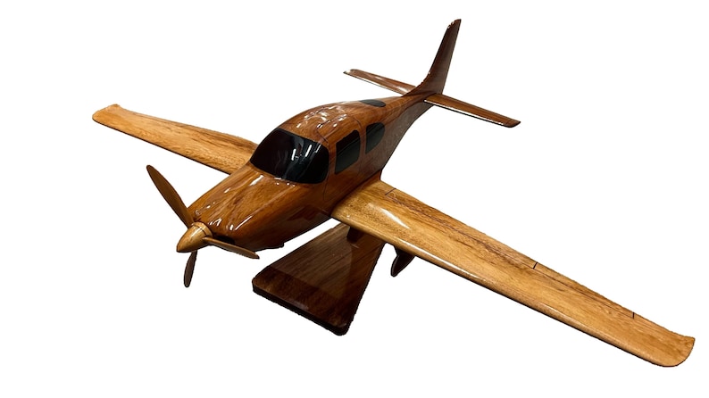 May include: A wooden model airplane with a brown and natural wood finish. The model is on a wooden stand and has a propeller.
