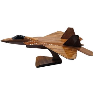 May include: A wooden model of a fighter jet, showcasing a detailed design with a glossy finish. The jet is brown with a black cockpit and is mounted on a wooden stand. The model is a decorative item.