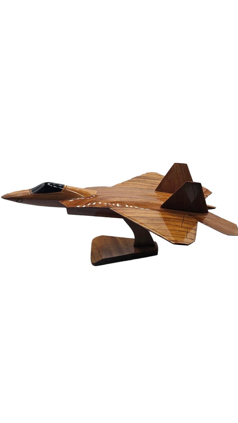 May include: A wooden model of a fighter jet, showcasing a detailed design with a glossy finish. The jet is brown with a black cockpit and is mounted on a wooden stand. The model is a decorative item.