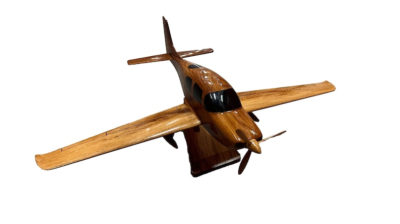 May include: A wooden model airplane with a brown and black paint scheme. The model is on a wooden stand and has a propeller.