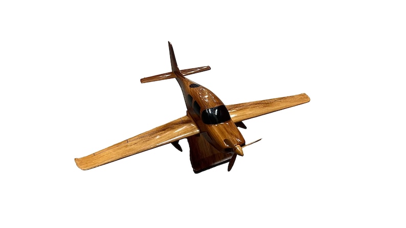 May include: A wooden model airplane with a brown and black paint scheme. The plane has a propeller and is in flight.