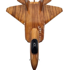 May include: A handcrafted wooden model of a jet fighter, showcasing a natural wood grain finish. The model features a detailed cockpit with a black interior and a sleek, aerodynamic design. The wings and tail fins are precisely carved, creating a realistic representation.