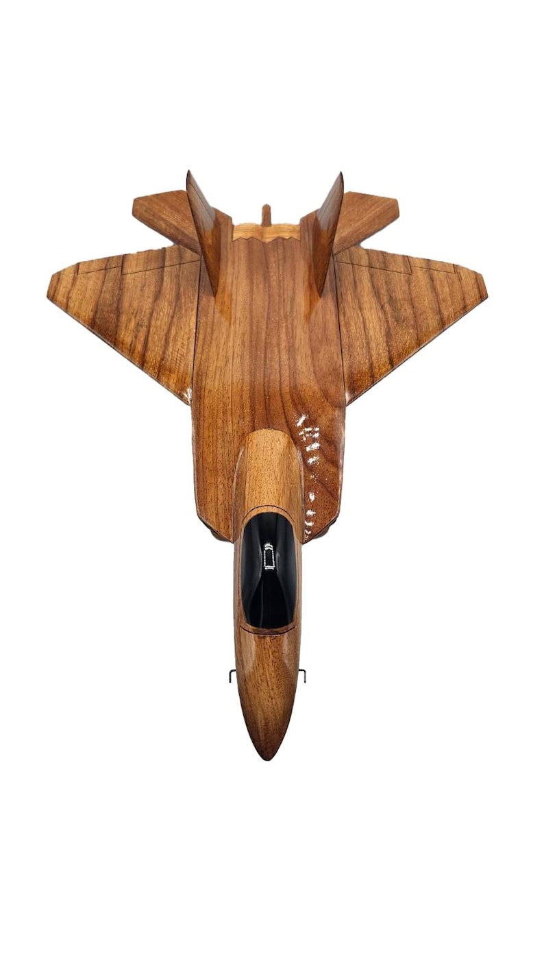 May include: A handcrafted wooden model of a jet fighter, showcasing a natural wood grain finish. The model features a detailed cockpit with a black interior and a sleek, aerodynamic design. The wings and tail fins are precisely carved, creating a realistic representation.