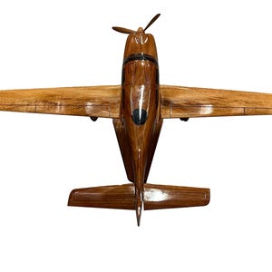 May include: A wooden model airplane with a brown wood finish. The airplane is in flight position with the wings spread out.