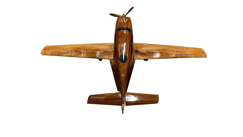 May include: A wooden model airplane with a brown wood finish. The airplane is in flight position with the wings spread out.