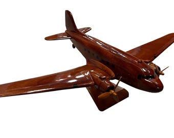 Könnte beinhalten: Ein detailliertes Holzmodellflugzeug mit einer satten, rotbraunen Oberfläche. Das Modell verfügt über zwei Propeller, Flügel und ein Heck, die alle präzise gefertigt sind. Das Flugzeug steht vor einem schlichten weißen Hintergrund.