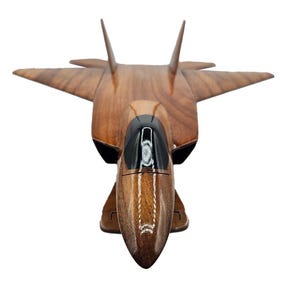 May include: A wooden model of a jet fighter aircraft. The model is made of a dark brown wood with a glossy finish. The cockpit is black, and the wings and tail are angled. The model is set against a white background.