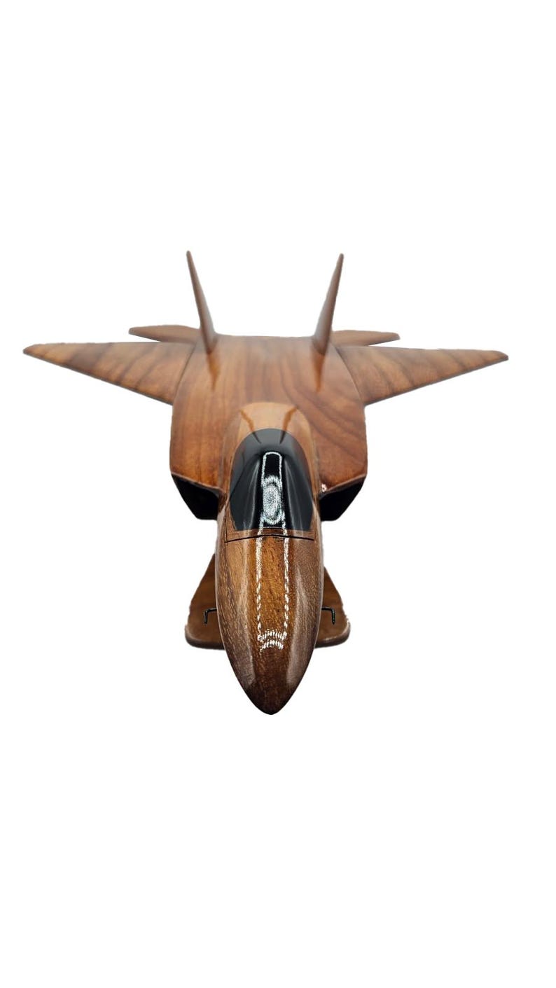 May include: A wooden model of a jet fighter aircraft. The model is made of a dark brown wood with a glossy finish. The cockpit is black, and the wings and tail are angled. The model is set against a white background.
