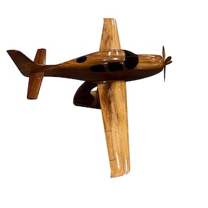 May include: A wooden model airplane with a brown and black paint scheme. The model is detailed with a propeller and windows.