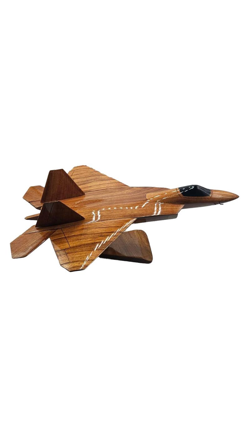 May include: A wooden model of a fighter jet, showcasing a detailed design with a brown finish and black cockpit. The wings and tail are angled, and the jet is mounted on a wooden stand. A decorative item.