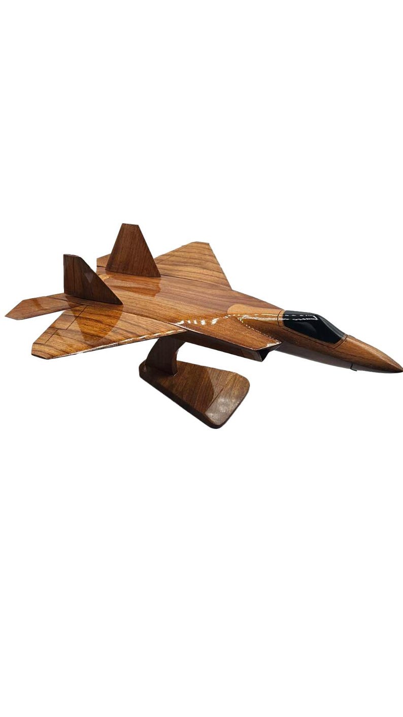 May include: A wooden model of a fighter jet, showcasing a detailed design with wings, tail fins, and a cockpit. The model is crafted from wood with a polished finish, mounted on a wooden stand.