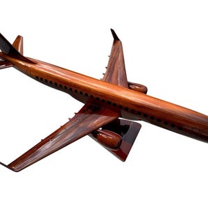Può includere: Un modello di aereo in legno con finitura lucida. Il modello è marrone con dettagli neri, tra cui finestre e dettagli delle ali. Le ali e la coda sono angolate e il modello è su sfondo bianco.