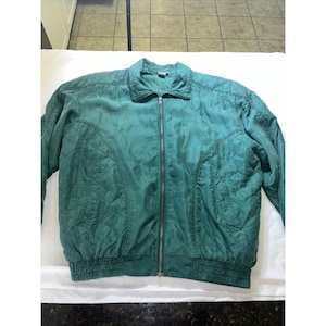 May include: A teal quilted jacket with a full zipper closure. The jacket features a ribbed hem and cuffs, a collared neckline, and diamond-shaped stitching patterns across the front and sleeves. The jacket is made of a shiny, lightweight material.
