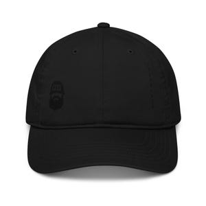 May include: A solid black baseball cap featuring a tonal embroidered graphic on the left front panel. The graphic depicts a stylized silhouette of a bearded figure wearing a hat with the text P24 inside. The cap has a curved brim and eyelets.