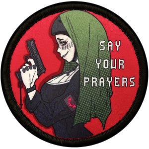 Op de afbeelding: Een geborduurde zwarte en groene patch met een vrouw die een pistool vasthoudt. De vrouw draagt een groene en zwarte hoofddoek. De tekst "SAY YOUR PRAYERS" staat in witte letters op een rode achtergrond.