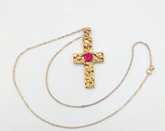 May include: A gold chain necklace with a textured gold cross pendant featuring a pink gemstone in the center.